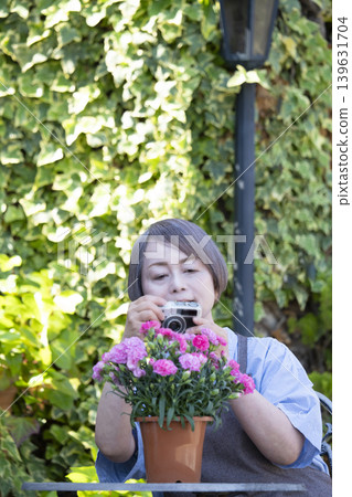 一位老婦人在自家院子裡侍弄花草時，正在拍攝花朵的照片。 139631704