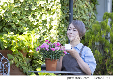 A senior woman drinking coffee while gardening in her yard. A senior woman drinking coffee while gardening in her yard. 139631947