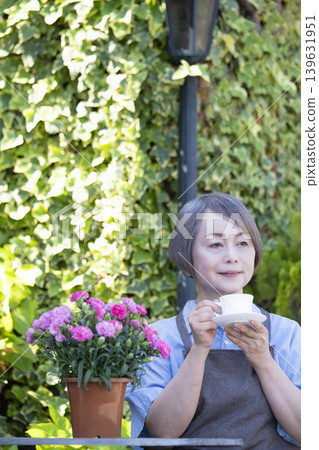 一位老婦人在自家院子裡一邊喝咖啡一邊種花。 一位老婦人在自家院子裡一邊喝咖啡一邊種花。 139631951