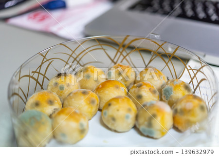 Mold growing on pastry balls in glass bowl showing spoiled food contamination and unsafe storage conditions in indoor environment 139632979