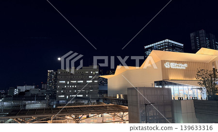 夜幕降臨,高輪站燈火通明,月光皎潔,展現出都市景觀的現代建築設計。 夜幕降臨,高輪站燈火通明,月光皎潔,展現出都市景觀的現代建築設計。 139633316