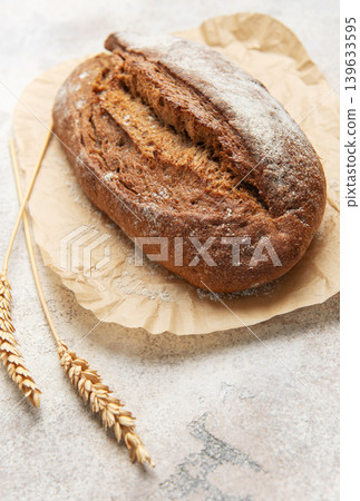 Rye bread loaf with wheat ears on parchment paper Rye bread loaf with wheat ears on parchment paper 139633595
