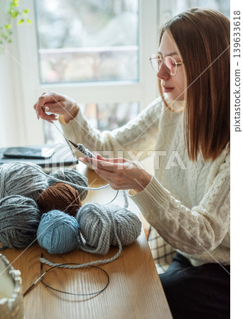 Woman knitting with yarn by window at home Woman knitting with yarn by window at home 139633618