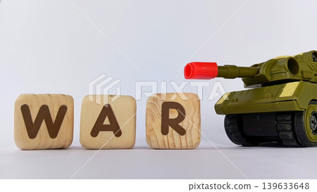 The text "WAR" on a cube or wooden block with miniature tanks and war trucks. World war illustration. The text "WAR" on a cube or wooden block with miniature tanks and war trucks. World war illustration. 139633648