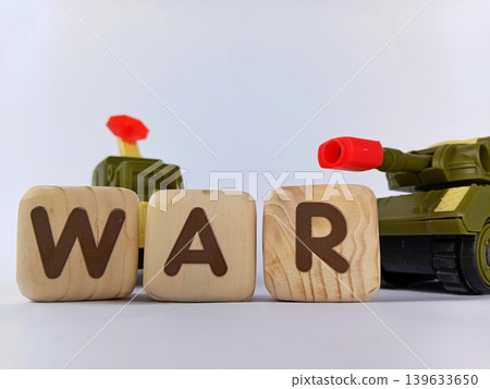 The text "WAR" on a cube or wooden block with miniature tanks and war trucks. World war illustration. 139633650