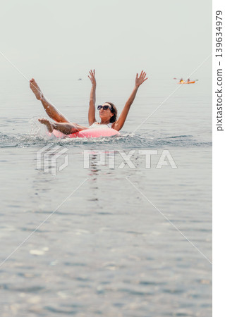 Woman inflatable ocean splashes in calm sea water with arms raised while enjoying a sunny summer vacation at the beach Woman inflatable ocean splashes in calm sea water with arms raised while enjoying a sunny summer vacation at the beach 139634979