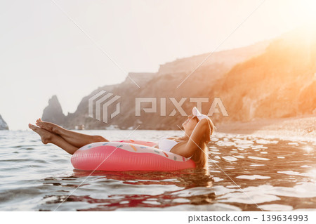 Woman, inflatable, ocean. Relaxed woman floating on a donut ring in the calm ocean at sunny sunset, copy space. Woman, inflatable, ocean. Relaxed woman floating on a donut ring in the calm ocean at sunny sunset, copy space. 139634993