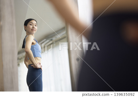 A middle-aged Japanese woman in yoga wear checks her figure in the mirror. A middle-aged Japanese woman in yoga wear checks her figure in the mirror. 139635092