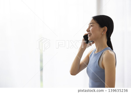 A Japanese woman in yoga wear smiles while talking on her smartphone. A Japanese woman in yoga wear smiles while talking on her smartphone. 139635236
