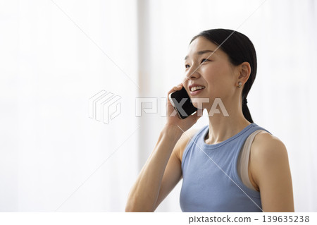 A Japanese woman in yoga wear smiles while talking on her smartphone. A Japanese woman in yoga wear smiles while talking on her smartphone. 139635238
