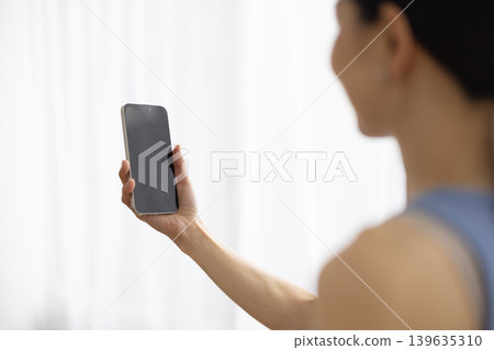 一位身穿瑜珈服的日本女子一邊用智慧型手機視訊通話一邊微笑。 139635310