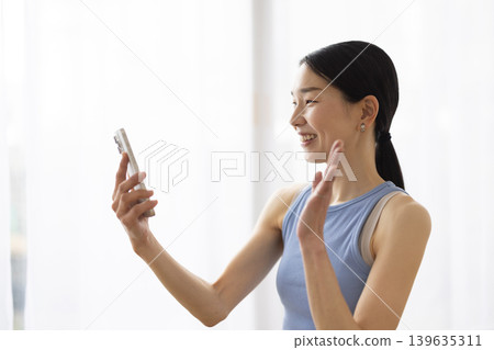 一位身穿瑜珈服的日本女子一邊用智慧型手機視訊通話一邊微笑。 139635311