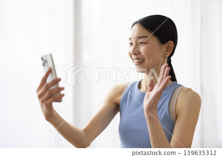 一位身穿瑜珈服的日本女子一邊用智慧型手機視訊通話一邊微笑。 139635312
