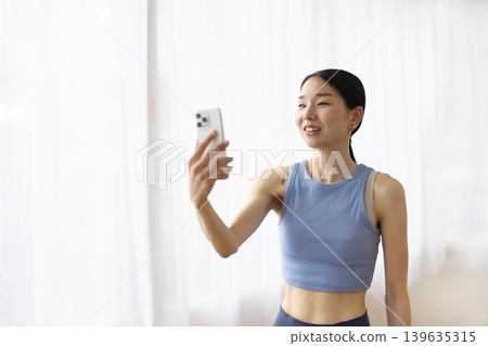 一位身穿瑜珈服的日本女子一邊用智慧型手機視訊通話一邊微笑。 139635315