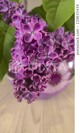 A bouquet of blooming lilacs with green leaves in a round glass vase A bouquet of blooming lilacs with green leaves in a round glass vase 139635434