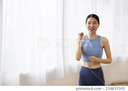 A middle-aged Japanese woman in yoga wear smiles by a bright window. A middle-aged Japanese woman in yoga wear smiles by a bright window. 139635505