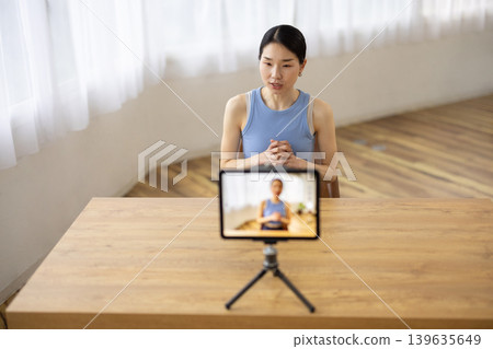A middle-aged Japanese woman in yoga wear talking in front of a tablet. A middle-aged Japanese woman in yoga wear talking in front of a tablet. 139635649
