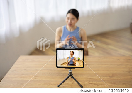 A middle-aged Japanese woman in yoga wear talking in front of a tablet. 139635650