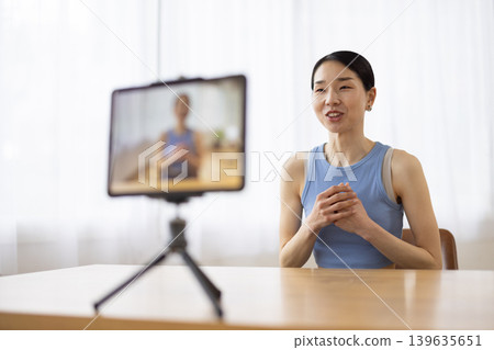 A middle-aged Japanese woman in yoga wear talking in front of a tablet. A middle-aged Japanese woman in yoga wear talking in front of a tablet. 139635651