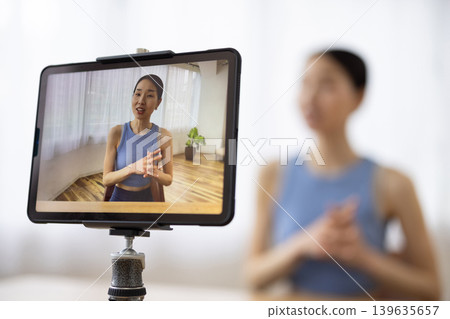 A middle-aged Japanese woman in yoga wear talking in front of a tablet. A middle-aged Japanese woman in yoga wear talking in front of a tablet. 139635657