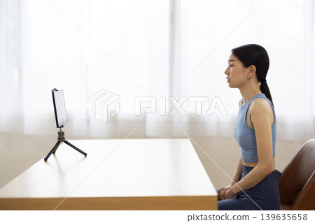 A middle-aged Japanese woman in yoga wear talking in front of a tablet. A middle-aged Japanese woman in yoga wear talking in front of a tablet. 139635658