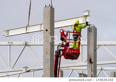 Construction worker aligning steel beam on concrete column using aerial lift and crane system Construction worker aligning steel beam on concrete column using aerial lift and crane system 139636168