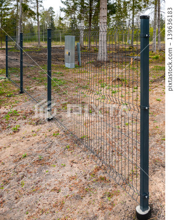 Metal mesh security fence, steel posts fixed in concrete-filled pipes buried in the ground Metal mesh security fence, steel posts fixed in concrete-filled pipes buried in the ground 139636183