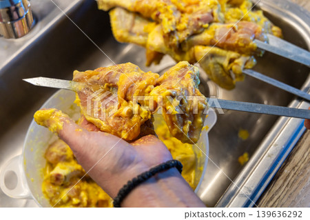 Man preparing marinated chicken skewers for barbecue grilling at home. Man preparing marinated chicken skewers for barbecue grilling at home. 139636292