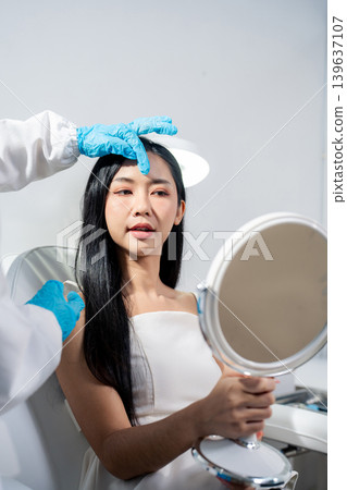 Asian woman consulting with a doctor at a modern aesthetic clinic for facial treatment. 139637107