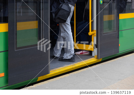 Passengers board a modern green tram at a city station, representing urban public transportation, efficient daily commuting, and sustainable mobility within a busy contemporary metropolitan area Passengers board a modern green tram at a city station, representing urban public transportation, efficient daily commuting, and sustainable mobility within a busy contemporary metropolitan area 139637119