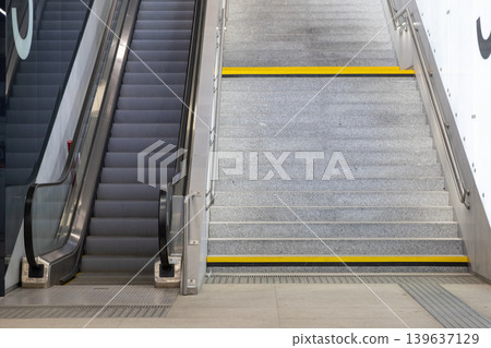 A modern escalator and concrete staircase with yellow safety stripes in a public station for urban transport, symbolizing convenient architecture and efficient travel connectivity in city life A modern escalator and concrete staircase with yellow safety stripes in a public station for urban transport, symbolizing convenient architecture and efficient travel connectivity in city life 139637129