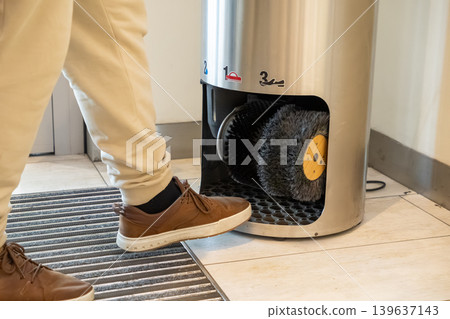 A professional person uses an automatic shoe polisher machine with rotating bristles in an office lobby to maintain leather footwear cleanliness and look sharp in a modern corporate setting A professional person uses an automatic shoe polisher machine with rotating bristles in an office lobby to maintain leather footwear cleanliness and look sharp in a modern corporate setting 139637143