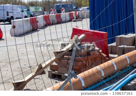A fenced construction site featuring metal fencing, orange safety barriers, and stacked building materials, representing urban development, infrastructure progress, and civil engineering standards A fenced construction site featuring metal fencing, orange safety barriers, and stacked building materials, representing urban development, infrastructure progress, and civil engineering standards 139637161