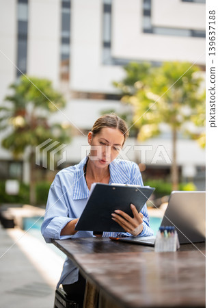 Female entrepreneur working remotely. Small business owner managing documents, laptop, and online success. Female entrepreneur working remotely. Small business owner managing documents, laptop, and online success. 139637188