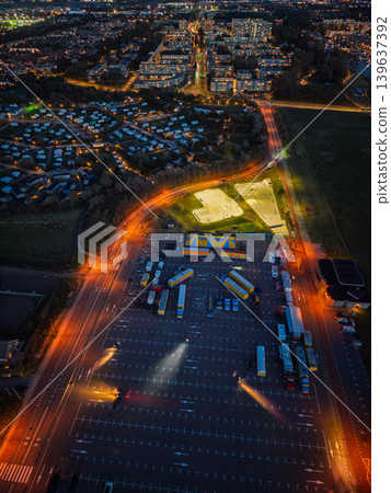 Aerial night view of a glowing cityscape in the Netherlands, featuring a circus camp in a large parking lot, a skate park, and residential districts illuminated by warm street lights. Aerial night view of a glowing cityscape in the Netherlands, featuring a circus camp in a large parking lot, a skate park, and residential districts illuminated by warm street lights. 139637392