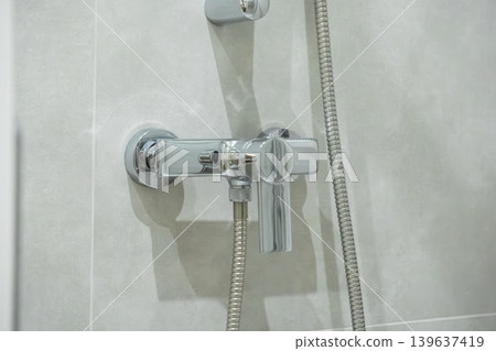 Modern chrome shower faucet mounted on light tiled wall representing contemporary bathroom interior design and plumbing hardware for residential or hotel home renovation projects Modern chrome shower faucet mounted on light tiled wall representing contemporary bathroom interior design and plumbing hardware for residential or hotel home renovation projects 139637419
