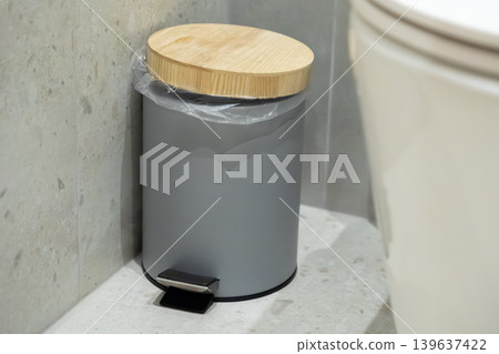 Modern grey pedal bin with a natural bamboo lid placed in a stylish bathroom corner to maintain cleanliness and promote organized waste disposal in a contemporary interior space Modern grey pedal bin with a natural bamboo lid placed in a stylish bathroom corner to maintain cleanliness and promote organized waste disposal in a contemporary interior space 139637422