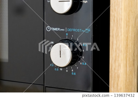 A close up view of a microwave timer knob with manual control dials for heating and defrost settings, representing modern domestic kitchen appliance usage for daily food preparation A close up view of a microwave timer knob with manual control dials for heating and defrost settings, representing modern domestic kitchen appliance usage for daily food preparation 139637432