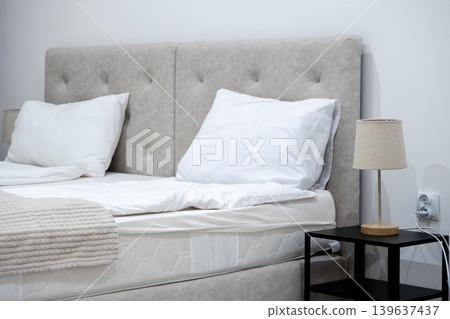 Modern upholstered bed with white pillows and matching bedside lamp, evoking luxury comfort in a clean contemporary bedroom interior design for relaxation and peaceful home rest Modern upholstered bed with white pillows and matching bedside lamp, evoking luxury comfort in a clean contemporary bedroom interior design for relaxation and peaceful home rest 139637437