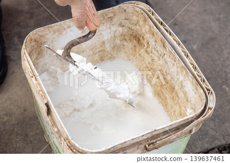 Trowel mixing white mortar in a plastic bucket on a construction site, emphasizing professional renovation preparation, manual labor, home improvement, and building material craft Trowel mixing white mortar in a plastic bucket on a construction site, emphasizing professional renovation preparation, manual labor, home improvement, and building material craft 139637461