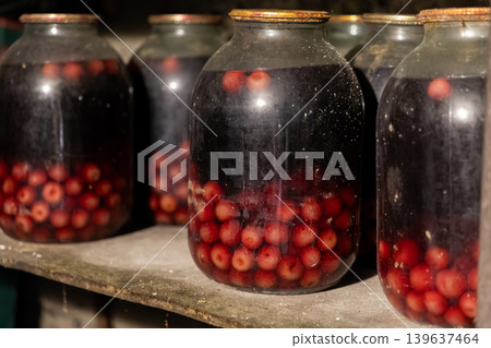 Glass jars filled with homemade preserved cherries sit on a rustic wooden cellar shelf, showcasing traditional canning methods and essential long-term food supplies for the winter Glass jars filled with homemade preserved cherries sit on a rustic wooden cellar shelf, showcasing traditional canning methods and essential long-term food supplies for the winter 139637464