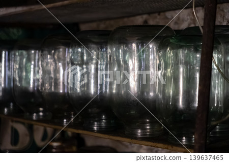 Row of empty glass jars lined up on a wooden shelf in a dark pantry, highlighting home food preservation, rustic kitchen storage solutions, and traditional rural life preparation Row of empty glass jars lined up on a wooden shelf in a dark pantry, highlighting home food preservation, rustic kitchen storage solutions, and traditional rural life preparation 139637465