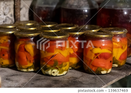 Glass jars with preserved bell peppers and spices sit on a rustic cellar shelf, representing homemade food supplies, traditional culinary methods, and sustainable pantry storage Glass jars with preserved bell peppers and spices sit on a rustic cellar shelf, representing homemade food supplies, traditional culinary methods, and sustainable pantry storage 139637469