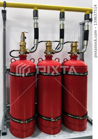 Three red gas cylinders connected to a yellow pipe in a workshop setting during daytime 139637514