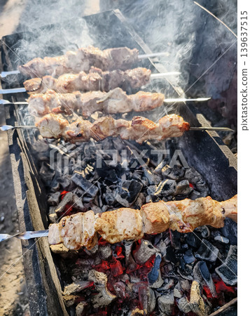 Grilling skewers of meat over open flames at a campsite during the afternoon hours 139637515