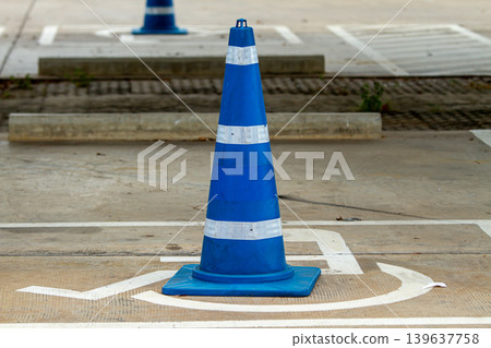 Blue traffic cone with reflective stripes placed on parking area for road safety and vehicle direction in an outdoor transportation setting. Blue traffic cone with reflective stripes placed on parking area for road safety and vehicle direction in an outdoor transportation setting. 139637758