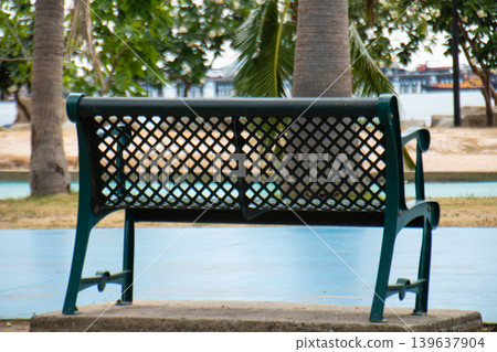 Empty metal bench in a tropical waterfront park surrounded by palm trees, offering a peaceful outdoor resting place with relaxing vacation atmosphere. Empty metal bench in a tropical waterfront park surrounded by palm trees, offering a peaceful outdoor resting place with relaxing vacation atmosphere. 139637904