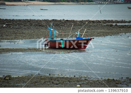 Fishing boat on muddy shore at low tide in calm coastal water, rustic wooden boat with nets and poles on tidal flat 139637910