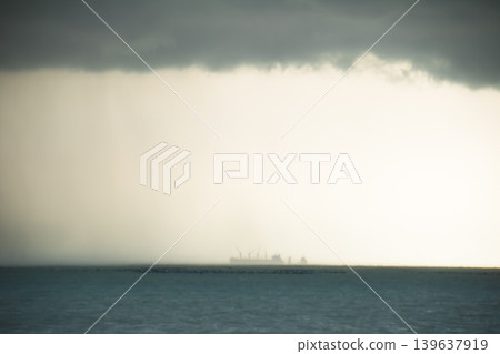 Storm cloud over sea horizon, distant ship in rain, moody seascape with dark sky and mist Storm cloud over sea horizon, distant ship in rain, moody seascape with dark sky and mist 139637919