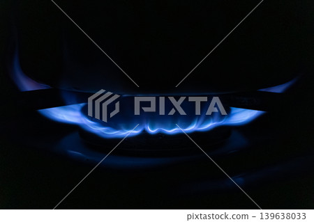 A bright blue gas flame burns on a modern stove burner in the dark, illustrating efficient heating, energy consumption, and essential cooking preparation for a daily kitchen life A bright blue gas flame burns on a modern stove burner in the dark, illustrating efficient heating, energy consumption, and essential cooking preparation for a daily kitchen life 139638033
